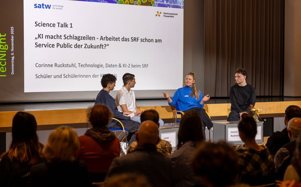 Panel discussion with three participants and a moderator on stage. The audience sits in front of it.