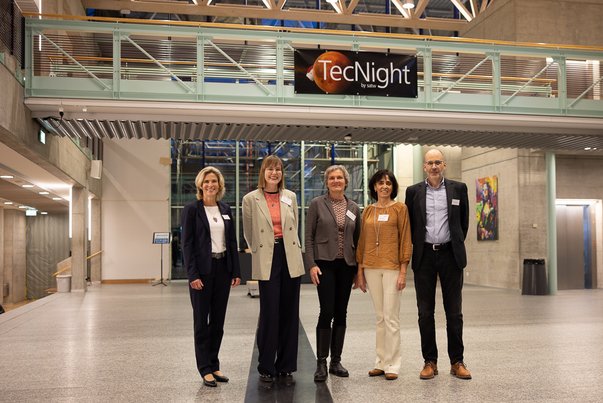 Five people stand in a modern building under a TecNight sign.