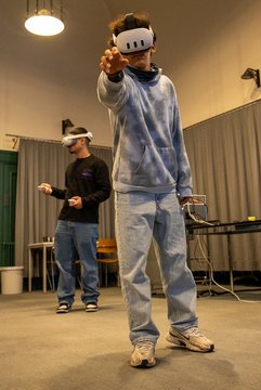 Boy wearing a VR headset reaches for something in the air. Another boy wearing a headset is in the background.