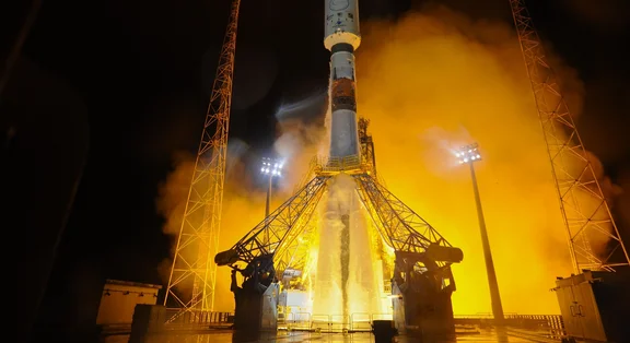 Rakete auf einer beleuchteten Startrampe bei Nacht, umgeben von orangefarbenem Rauch und Dampf.