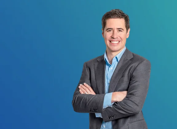 Manuel Kugler, Programme Manager Data &amp; AI / Advanced Manufacturing, in a grey suit against a blue background