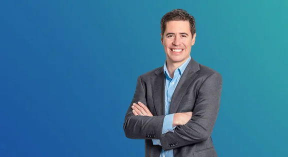 Manuel Kugler, Programme Manager Data &amp; AI / Advanced Manufacturing, in a grey suit against a blue background