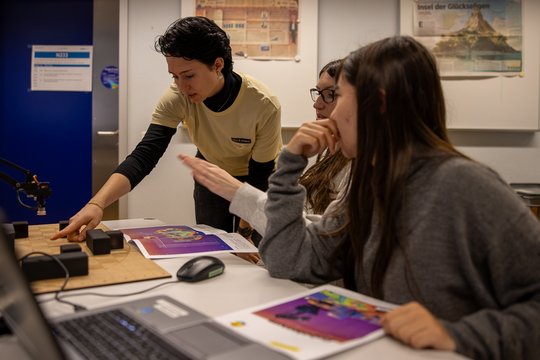 A woman shows two schoolgirls something on the table.
