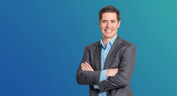 Manuel Kugler, Programme Manager Data &amp; AI / Advanced Manufacturing, in a grey suit against a blue background