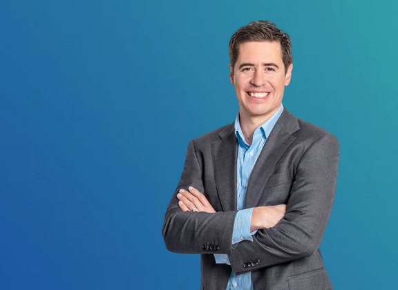 Manuel Kugler, Programme Manager Data &amp; AI / Advanced Manufacturing, in a grey suit against a blue background